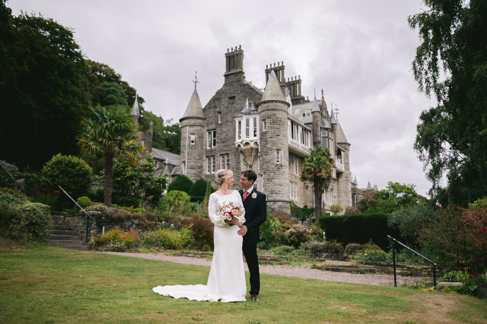 Bride & Groom stand in front of Chateau Rhianfa and look at each other during wedding photography