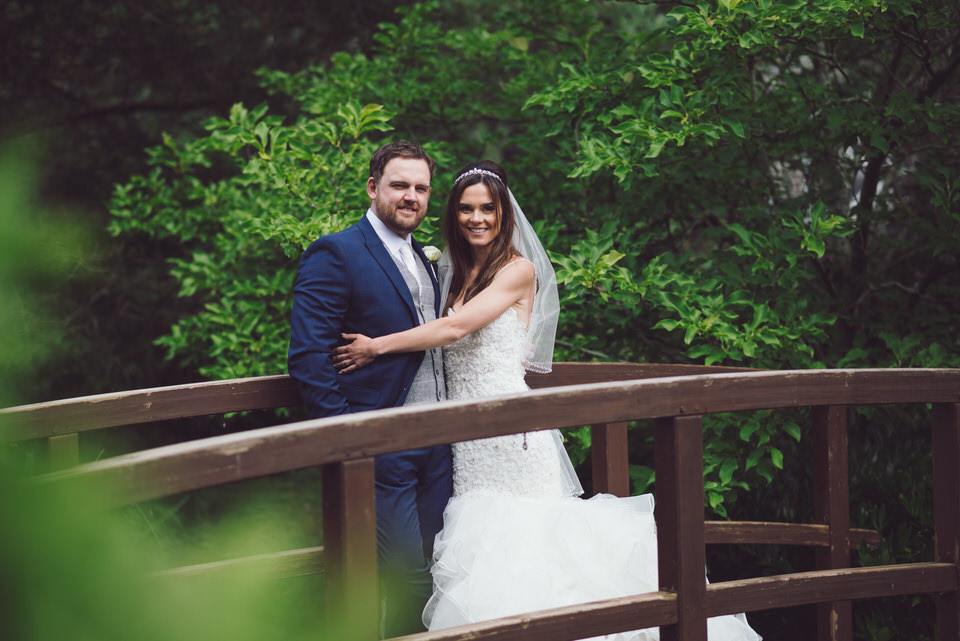 Bride & Groom embrace on a wooden bridge outside of the Wild Pheasant wedding venue 