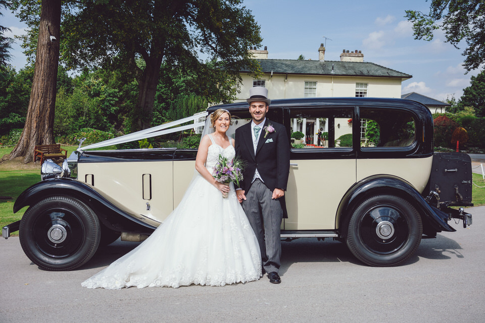 Bride & Groom stand in front of vintage car with Highfield hall in background