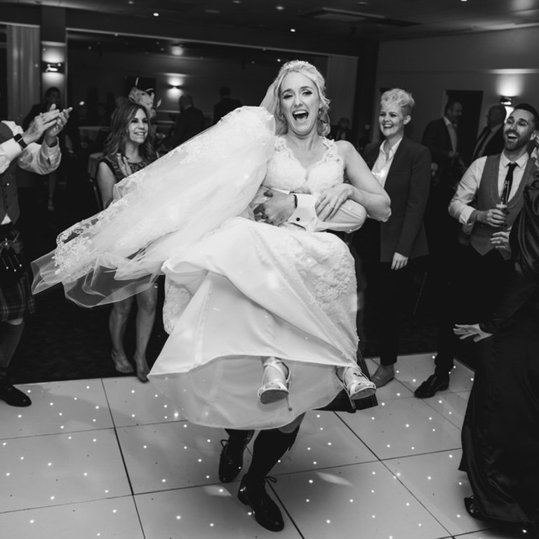 Bride is lifted in the air and smiles on the dancefloor at a local Wedding venue near me