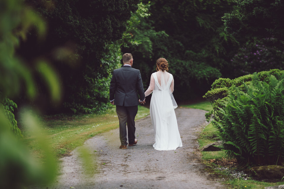 Bride & Groom walk away down path at Harrisons Hall holding hands