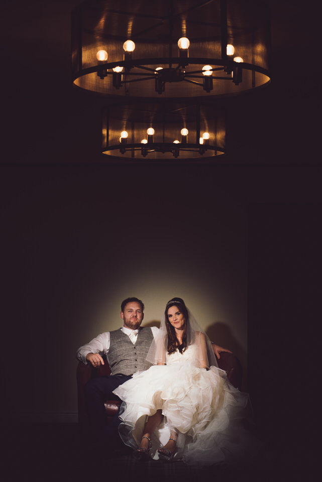 Bride & Groom sit down and pose for photograph with spotlight on them at Wild Pheasant hotel