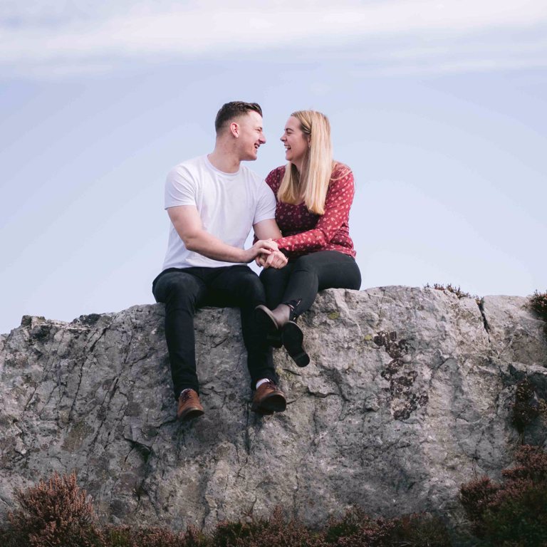 Engaged couple sitting on top of Hope Mountain North Wales