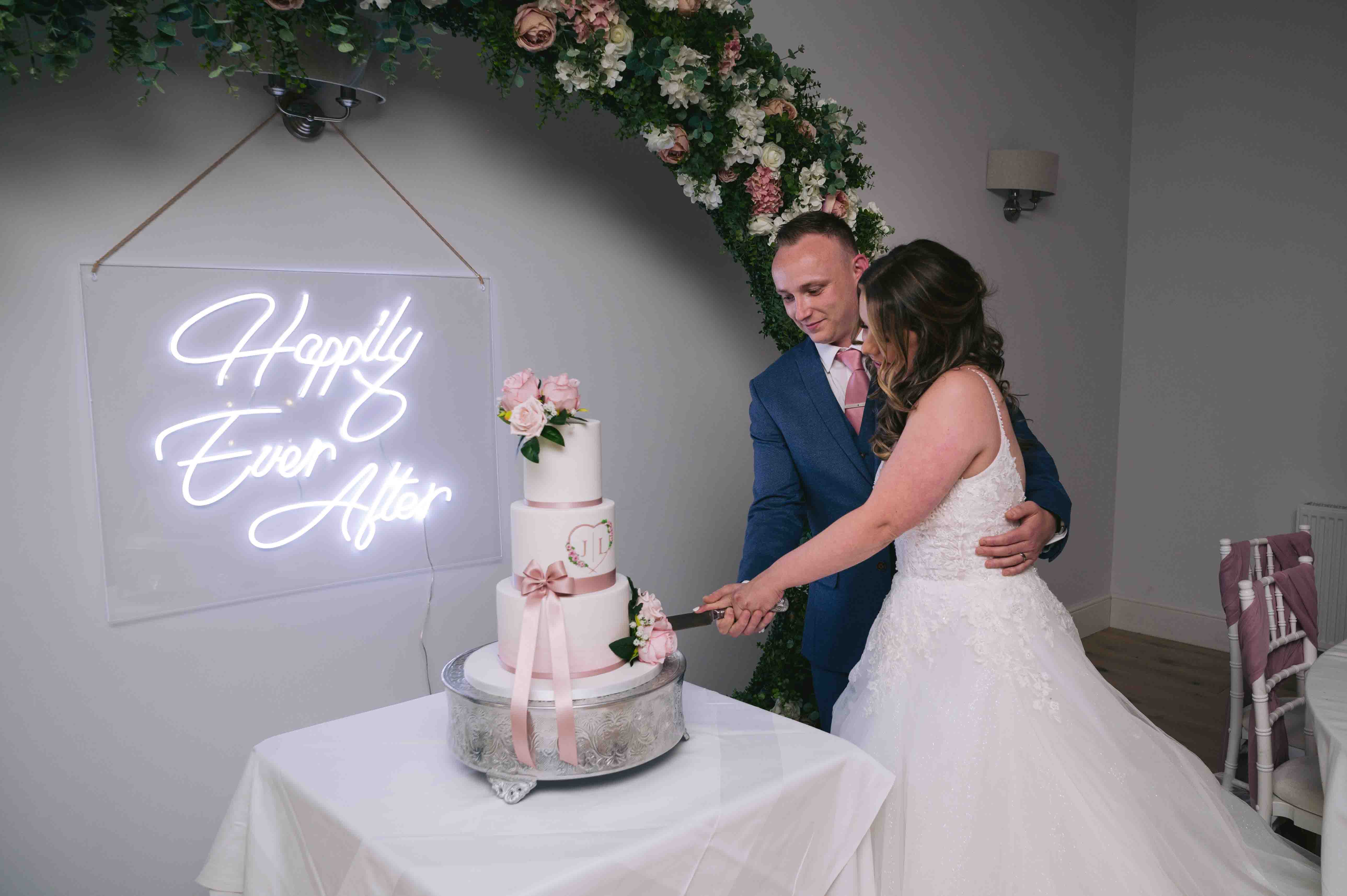 Bride & Groom cut wedding cake in front of a neon sign at Highfield Hall