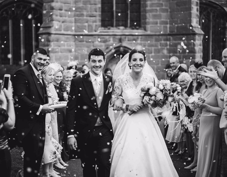 Couple smile during confetti shot outside church wedding in Cheshire