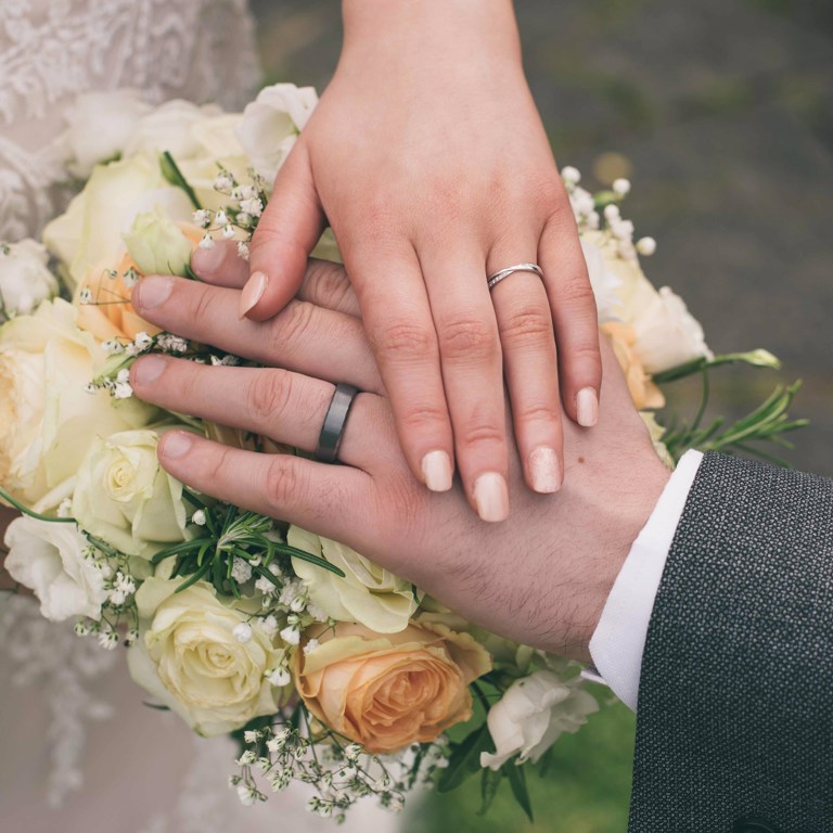 Close up photo of Bride & Grooms hands & wedding rings on top of bouquet of flowers