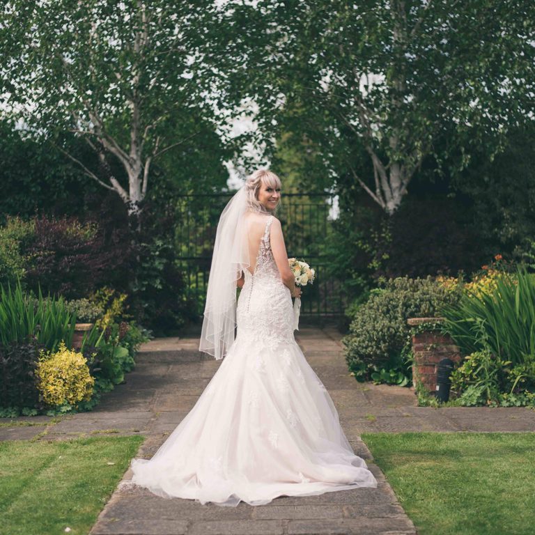 Bride stands in gardens at Lion Quays and smiles back at the camera