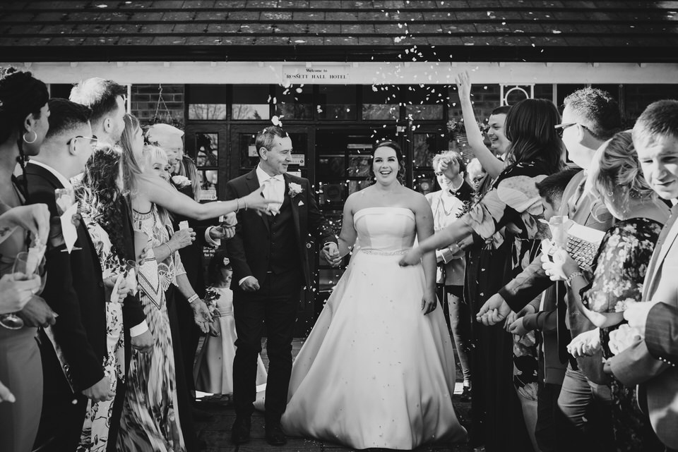 Bride & Groom walk between guests throwing confetti at Rossett Hall Hotel Cheshire