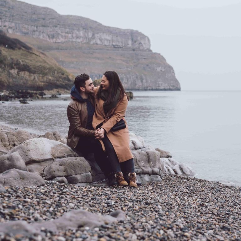 Engaged couple sat on rock near sea in North Wales