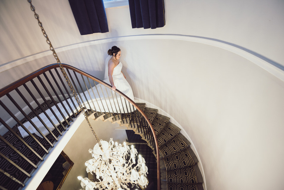 Bride walks down winding staircase in wedding dress at Rossett Hall Hotel