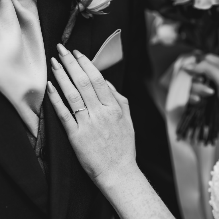 Bride places hand on grooms lapel, showing engagement ring