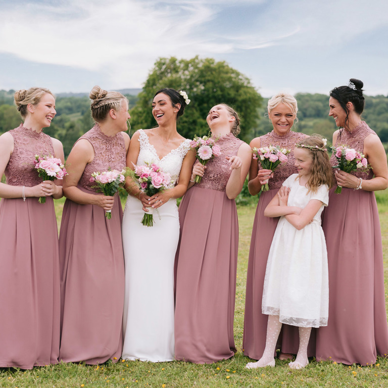 Bride & Bridesmaids laugh during marquee local wedding in a field with blue skies