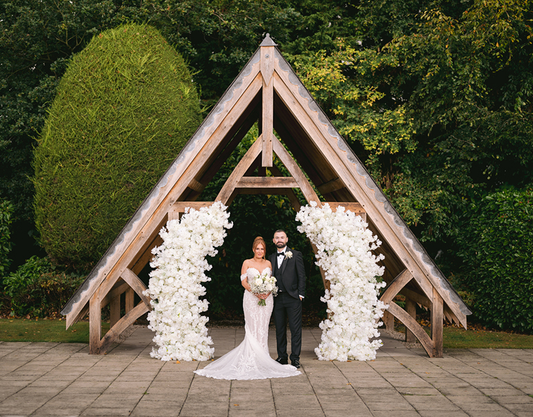 Bride and Groom stand under the Pergoda with a floral display at Highfield Hall wedding during photography