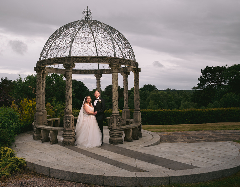 Bride and groom stand under pergoda at their wedding at Hillbark Hotel near Chester