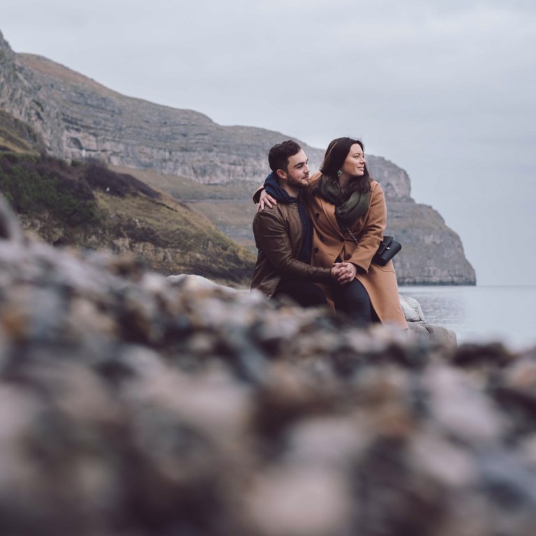 Engaged couple sat on rock overlooking sea in North Wales