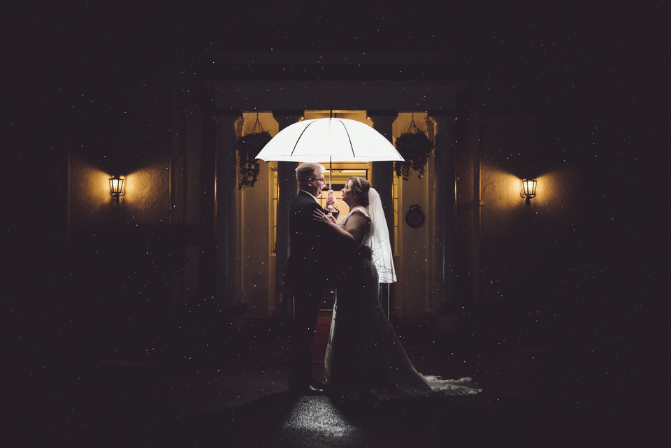 Bride & Groom outside Highfield hall wedding venue at night time, holding umbrella