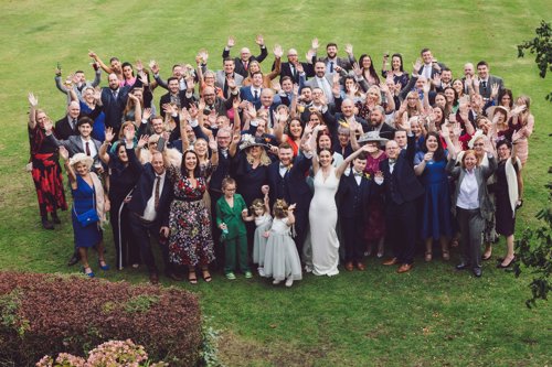 Wedding guests throw their hands in the air and smile during big group photograph