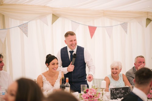 Bride & Groom laugh during wedding speeches in Marquee in Ruthin