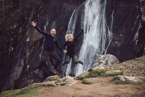 Couple jump in the air in front of waterfall on pre wedding shoot in North wales