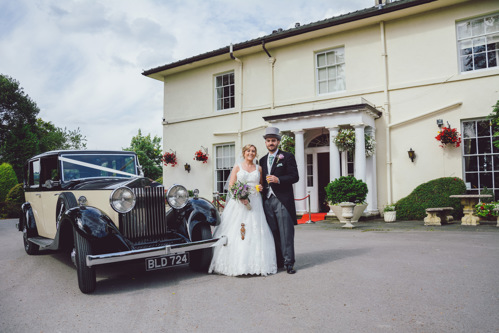 Bride & Groom stand in front of classic car with Highfield Hall wedding venue in the background