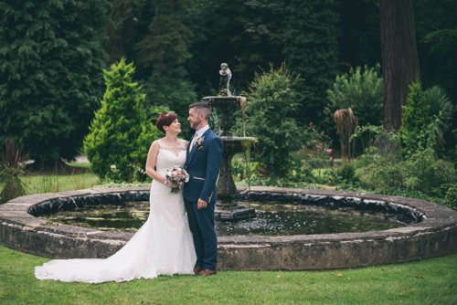 Bride and groom stand in front of fountain at Highfield Hall North Wales