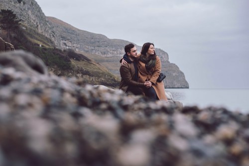 Couple sit on rock and look out towards Llandudno sea during pre wedding shoot in North Wales